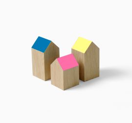 Drie houten blokjes in de vorm van een huisje met schuine daken gekleurd in roze, blauw en geel